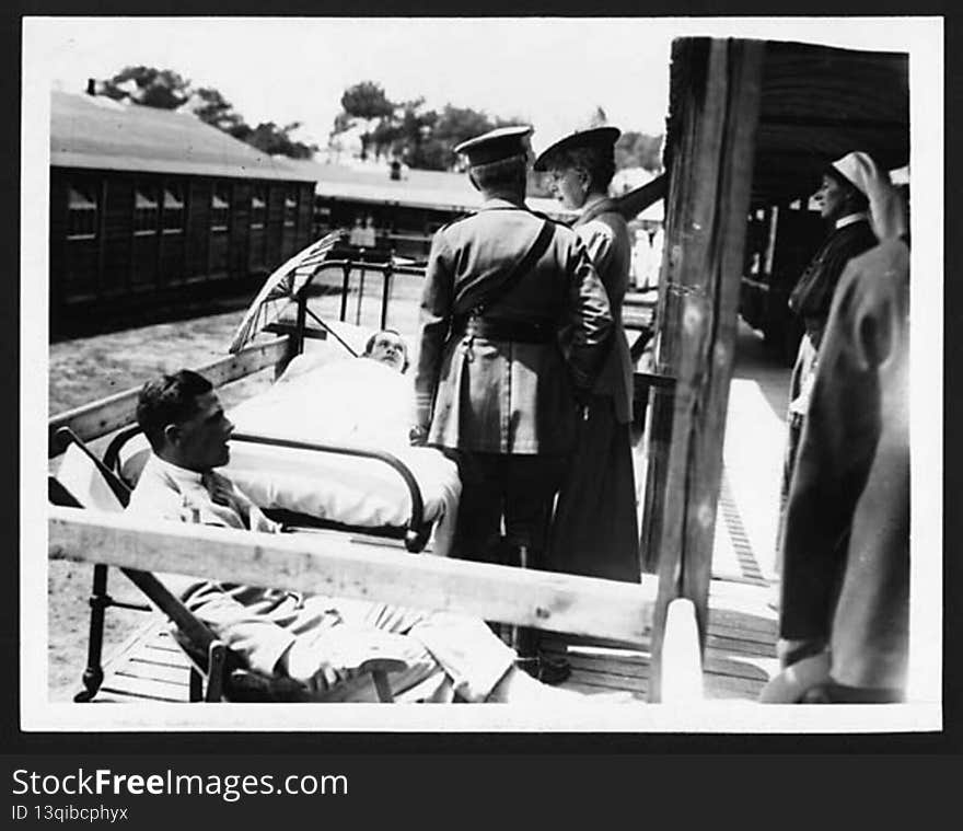 Queen Mary visiting a hospital on the Western Front. She is standing outside on a wooden balcony talking to a wounded soldier. He is lying on a bed with a sunshade propped up beside his head, to protect his face from the sun. There is a man sitting on a deckchair at the end of the bed, possibly another patient. A uniformed man stands next to the Queen, and a nurse watches the scene from the background. 

King George V and Queen Mary visited the Western Front on a number of occasions during World War I. Queen Mary spent a lot of her time visiting sick and wounded soldiers in hospitals behind the front line. An important function of royal visits was to raise the spirits of those involved in every aspect of the war.

[Original reads: .&#x27;.ON THE BRITISH WESTERN FRONT. THE VISIT OF HER MAJESTY THE QUEEN. - THE QUEEN CHATS WITH A PATIENT.&#x27;]

digital.nls.uk/74546706