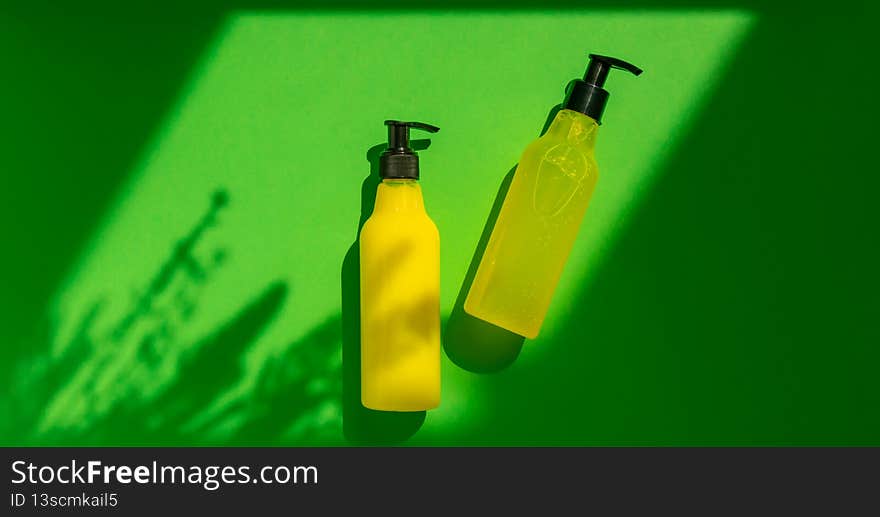 Plastic mock-up of yellow cosmetic bottles with shadow flowers on a green background. A creative, minimalistic snapshot of a