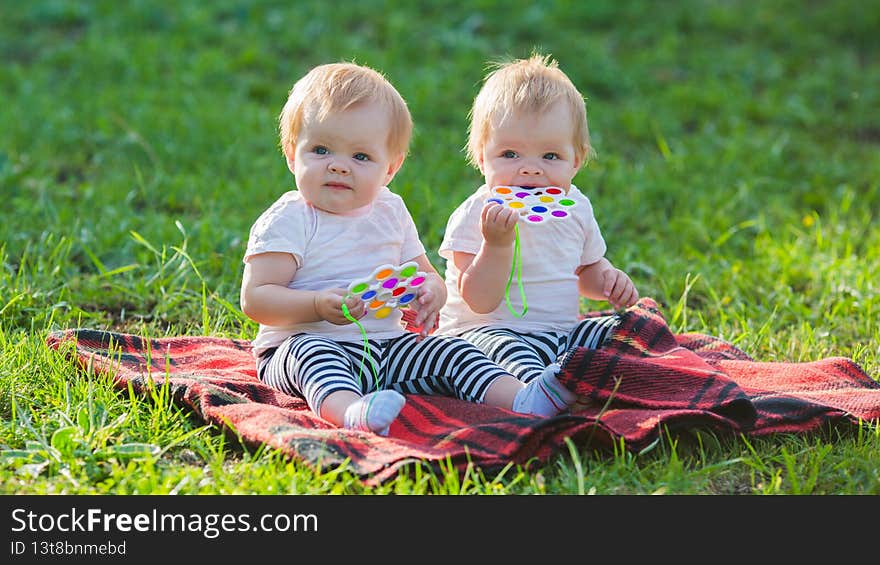Two twin girls play with colored toys a blanket