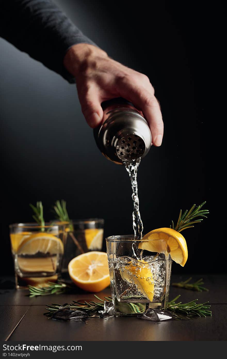 Cocktail Gin and Tonic with lemon and rosemary. The bartender pours a cocktail from a shaker into a glass