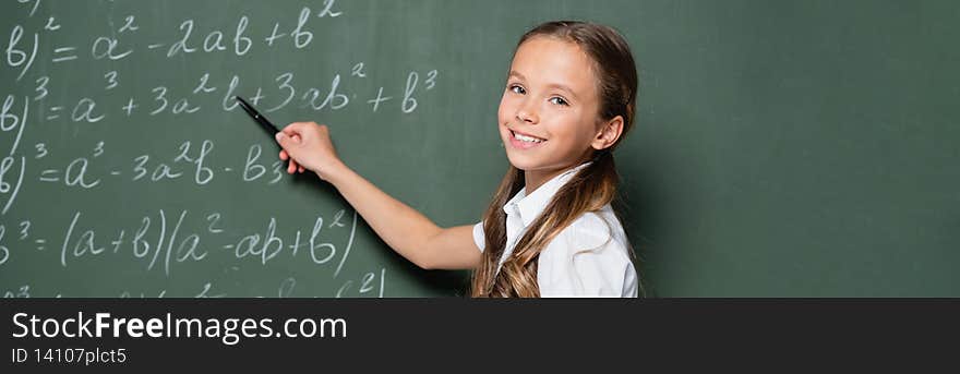 schoolgirl smiling at camera while pointing at equations on chalkboard, banner,stock image