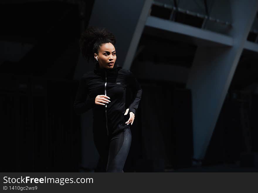 African american sportswoman in earphone running on urban street,stock image