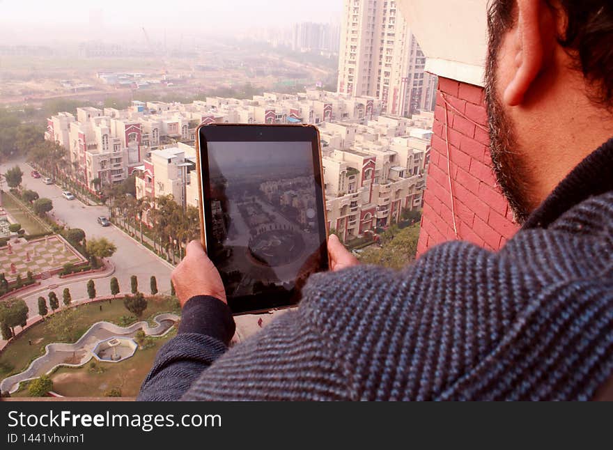 A guy photographing from the top of the building with his ipad. below are the buildings which tiny as compared to the building from where this photograph has been taken. A guy photographing from the top of the building with his ipad. below are the buildings which tiny as compared to the building from where this photograph has been taken.
