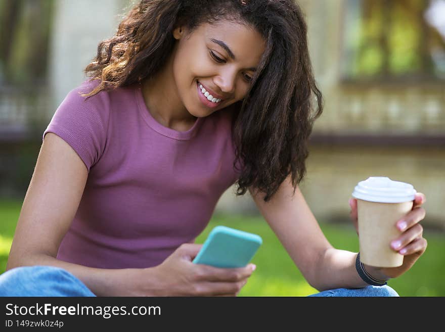 A cute girl in a pink tshirt sitting on the grass and having coffee