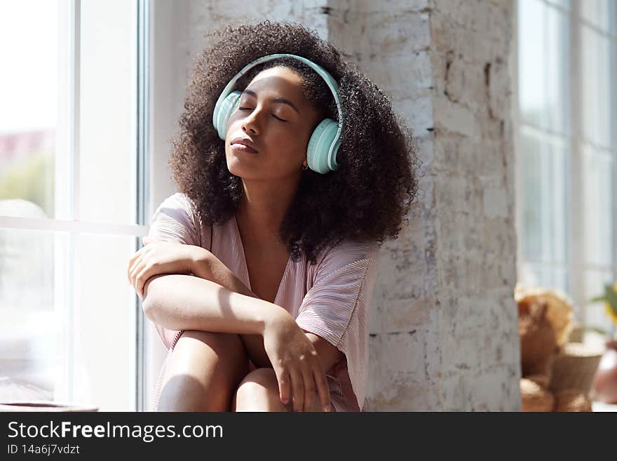 A gorgeous mixed-race woman is captivated by the pleasant sensations as she listens to relaxing music on her phone. A break from freelance work, as well as a search for inspiration and creativity
