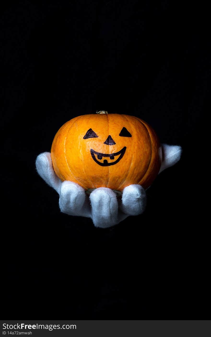 Hand in a white glove holds a pumpkin on a black background