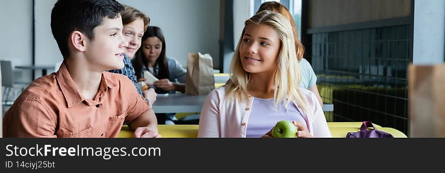 happy teenage friends talking in school dining room near classmates, banner,stock image