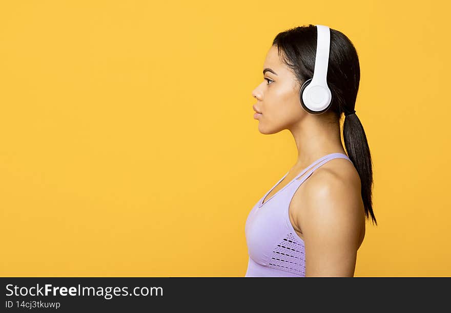 Motivation, music for workout. Young african american female with headphones looking at free space, yellow background