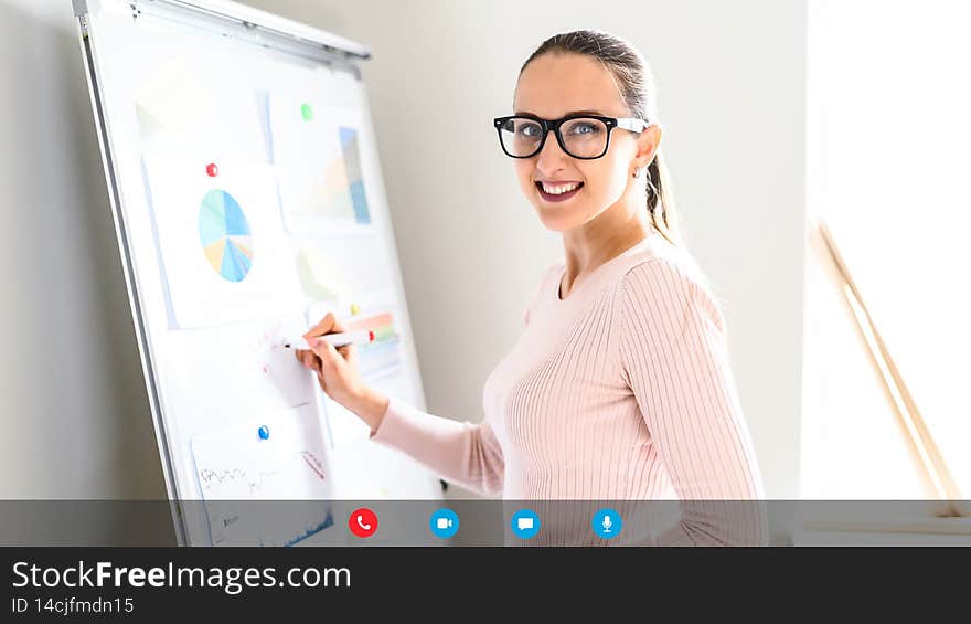 Smart and confident female employee holding online presentation, stands near whiteboard and explain information to online audience, video screen, video meeting, conference or webinar on the distance
