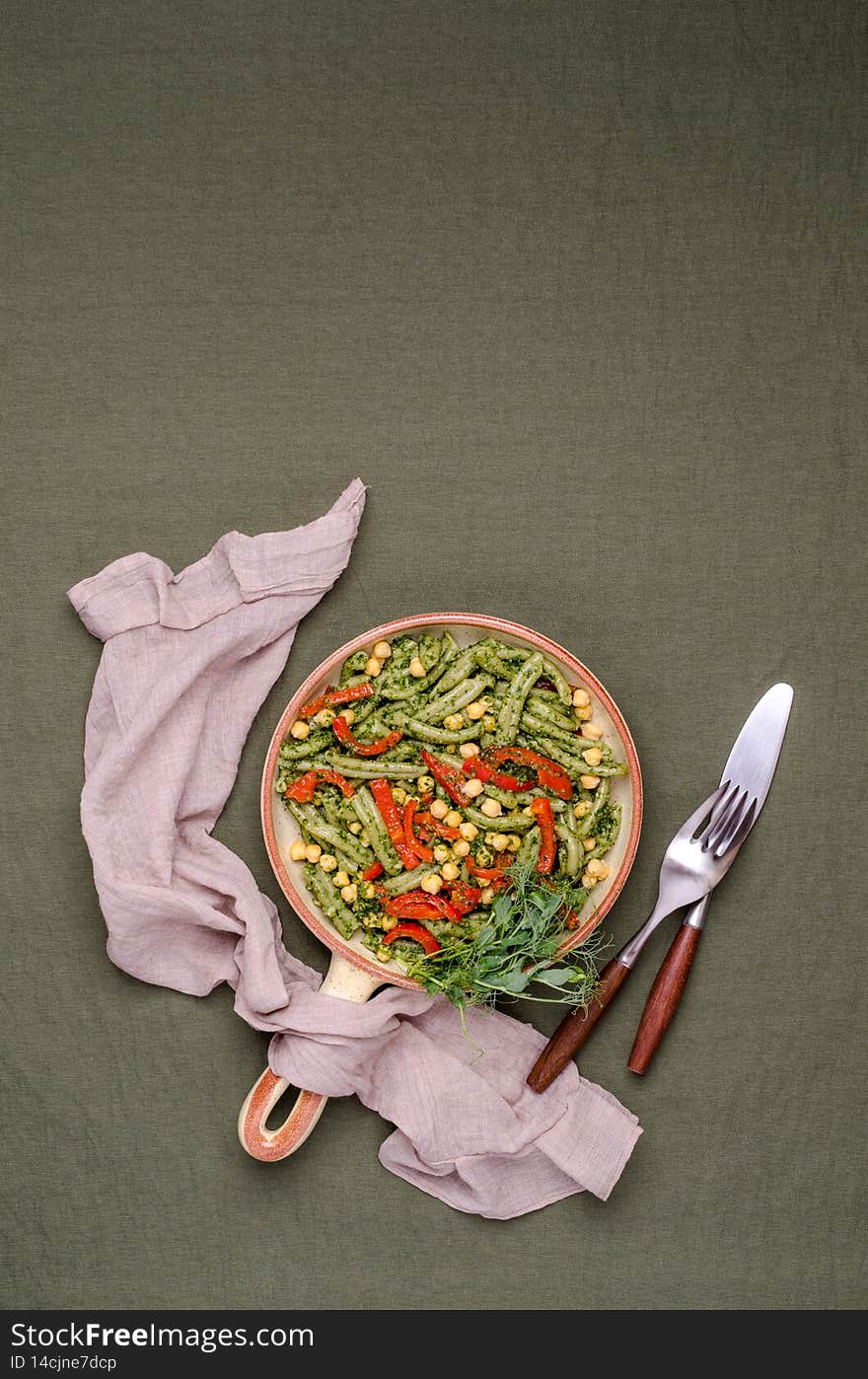Green pasta with chickpeas, pepper and pesto sauce on a textile background. Top view. Selective focus