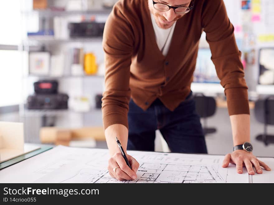 Male Architect Standing At Desk In Office Amending Building Plans