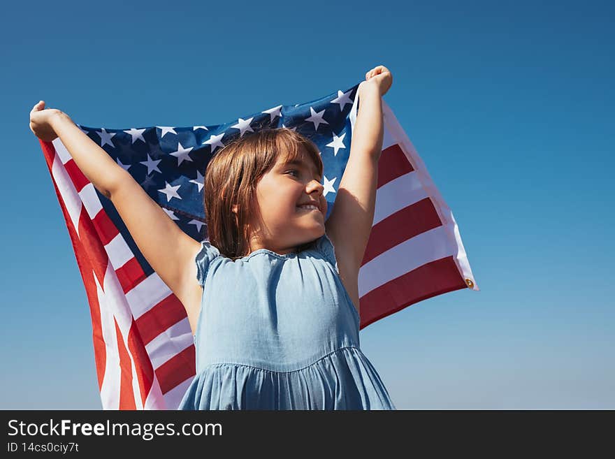 Portrait of a happy girl with the American flag in her hands against the background of the sky