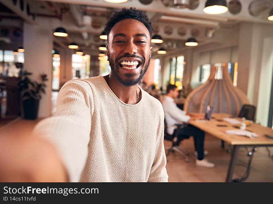 Portrait Of Young Businessman Taking Selfie On Mobile Phone In Modern Open Plan Office