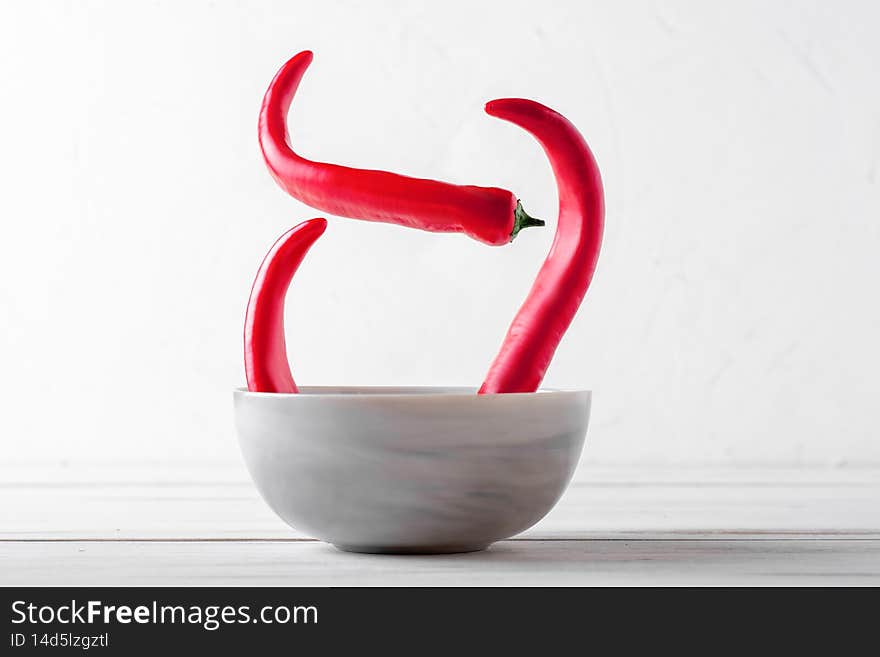 Spicy food concept with red pepper. Soup plate with chili peppers on a white wooden background.