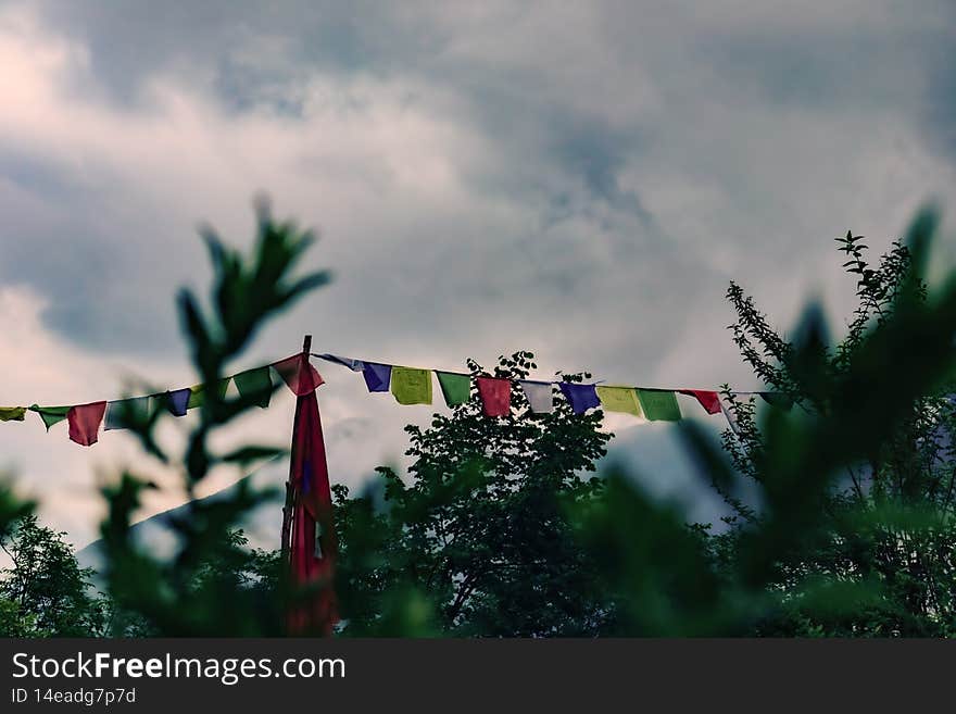 Colored tibetan flags. Vegetation on the foreground. Clouds and mountains on the background. Concept of tibetan culture, buddhism