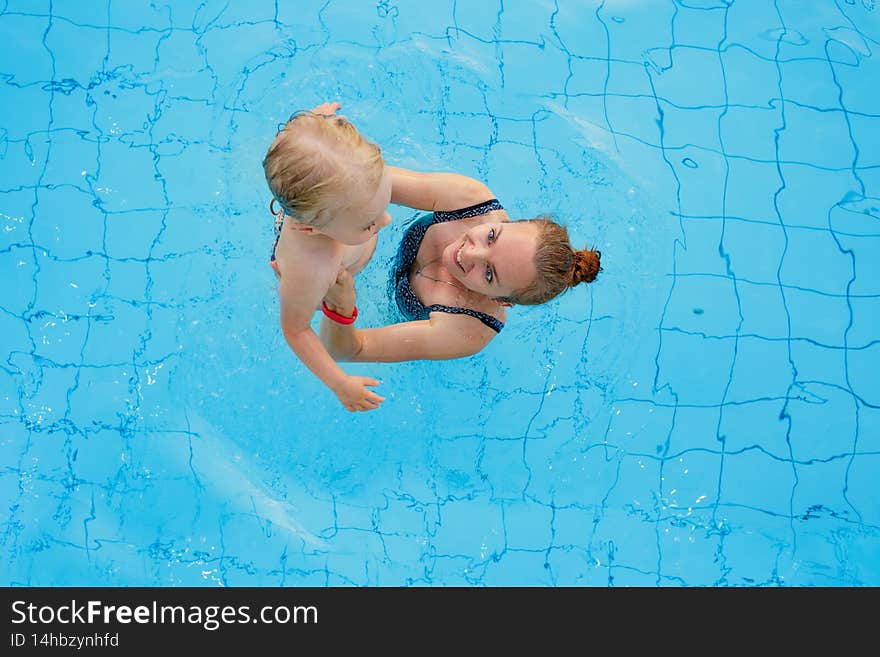 Mother and baby in outdoor swimming pool of tropical resort. Kid learning to swim. Mom and child playing in water. Family summer vacation in exotic destination. Active and healthy sport for kids. Mother and baby in outdoor swimming pool of tropical resort. Kid learning to swim. Mom and child playing in water. Family summer vacation in exotic destination. Active and healthy sport for kids.