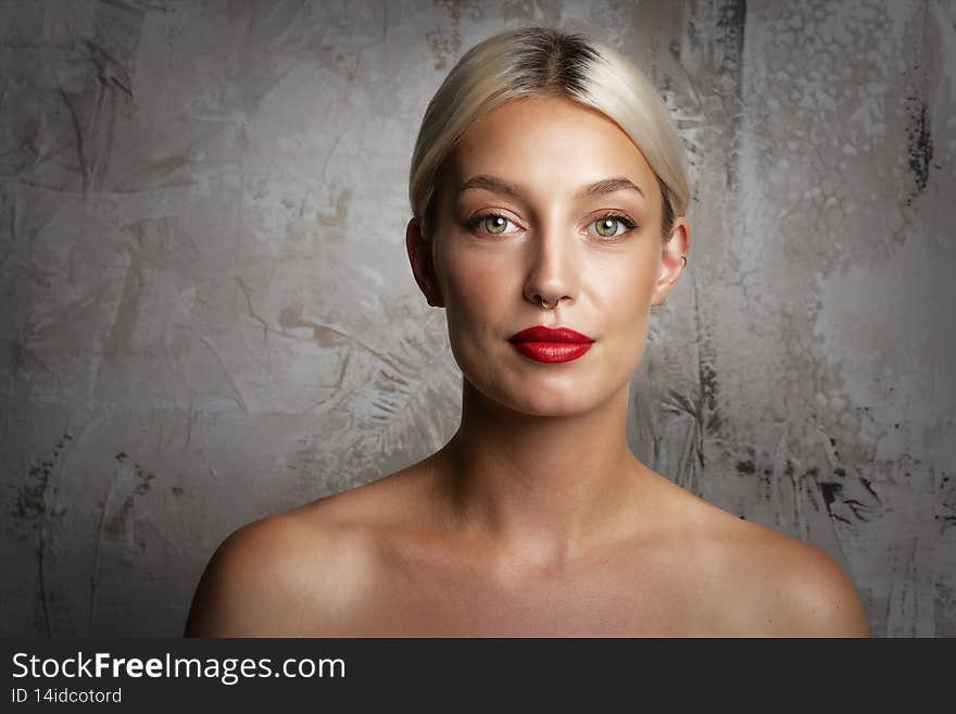 Headshot of gorgeous young woman with blond hair wearing red lipstick and nose piercing while standing at isolated dark grey background. Headshot of gorgeous young woman with blond hair wearing red lipstick and nose piercing while standing at isolated dark grey background