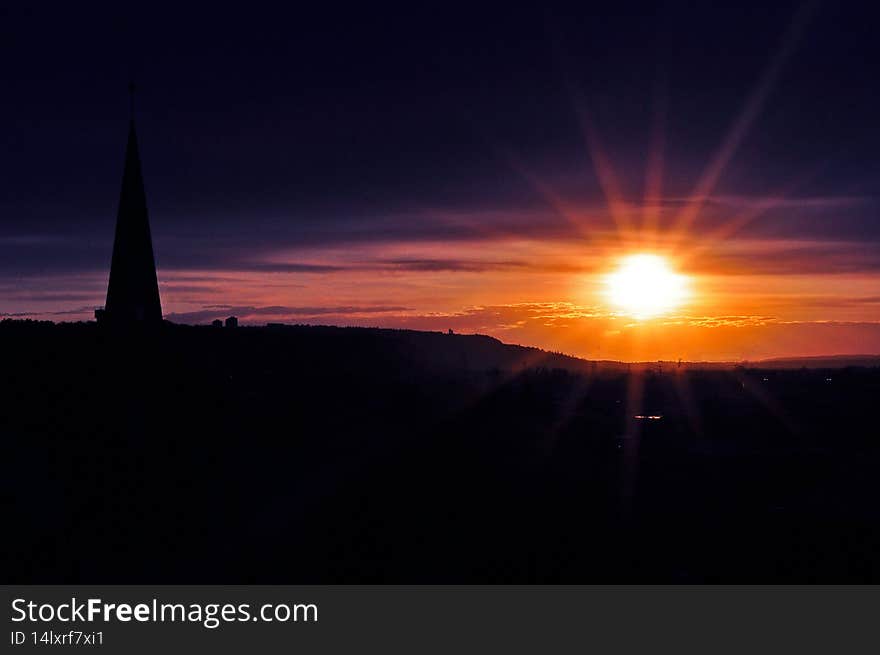 A bright and colourfuol sunset decorates the sky as a church steeple lines the foreground. A bright and colourfuol sunset decorates the sky as a church steeple lines the foreground