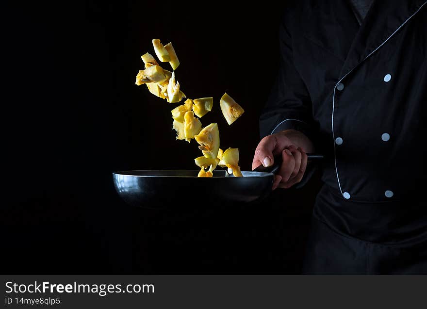 A professional chef prepares zucchini in a pan. Cooking vegetables healthy vegetarian food and meal on a dark background. Free ad space.