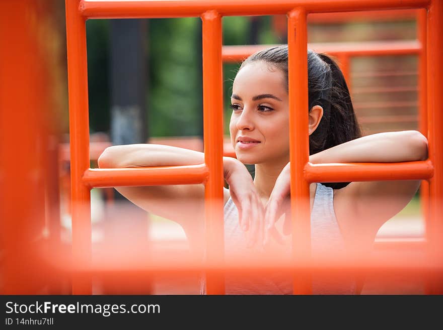 smiling sportswoman looking away near orange vertical ladder outside,stock image