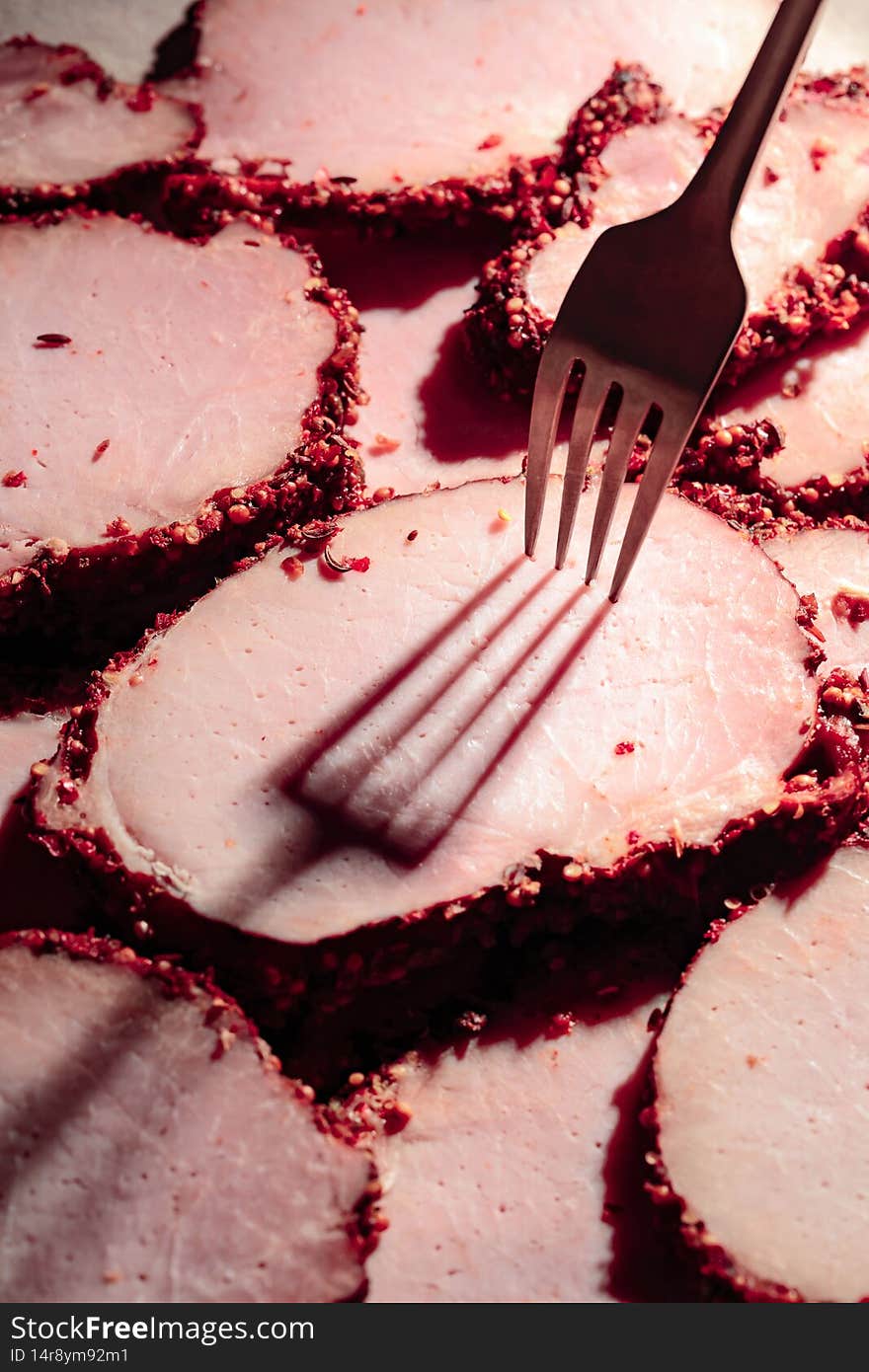 Slices of spicy smoked ham and fork with long shadow. Selective focus