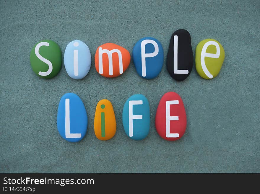 Simple Life, creative motivational slogan composed with multi colored stone letters over green sand