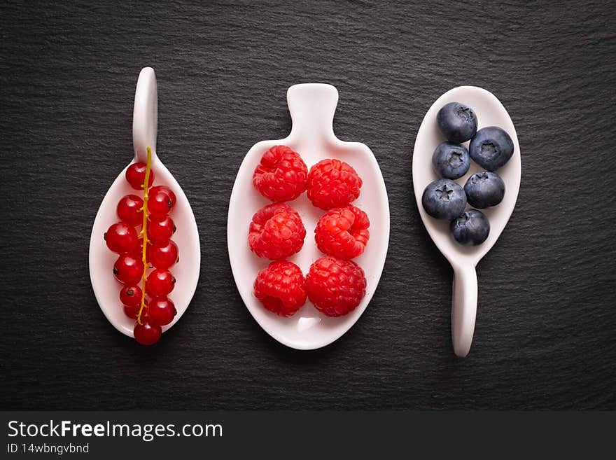 Ripe berry - raspberries, red currants and blueberries, lie in a white dish