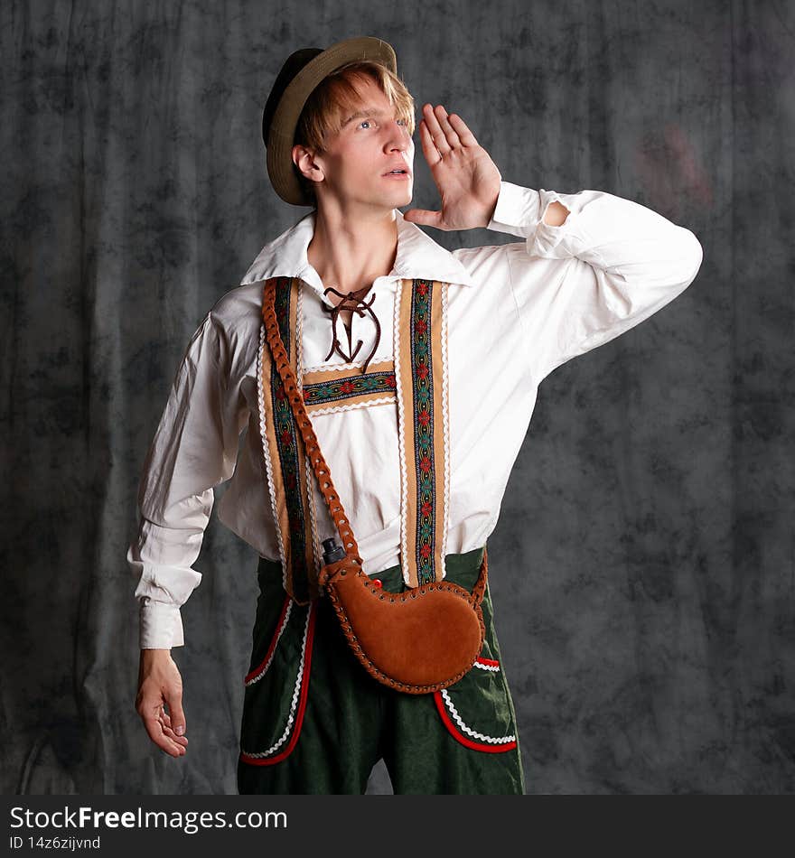 A young man in a national Bavarian suit with shorts on suspenders and a hat.