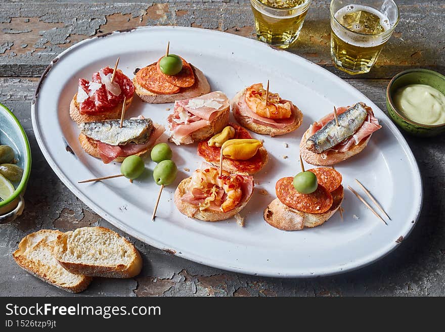 From above of plate with appetizing bruschettas with seafood and meat served on wooden table with beer. From above of plate with appetizing bruschettas with seafood and meat served on wooden table with beer