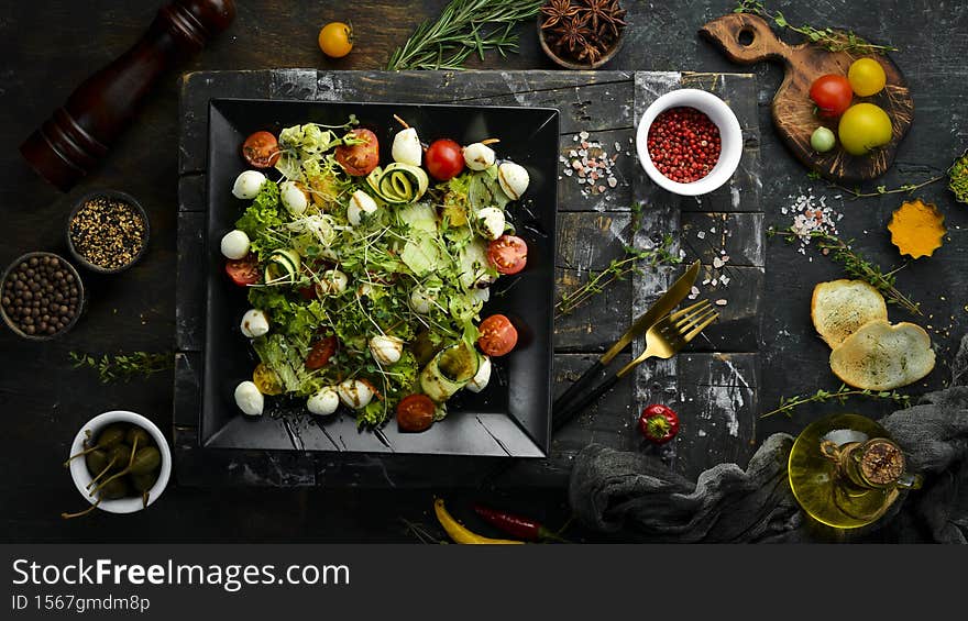 Vegetable salad with mozzarella cheese. On a black plate.