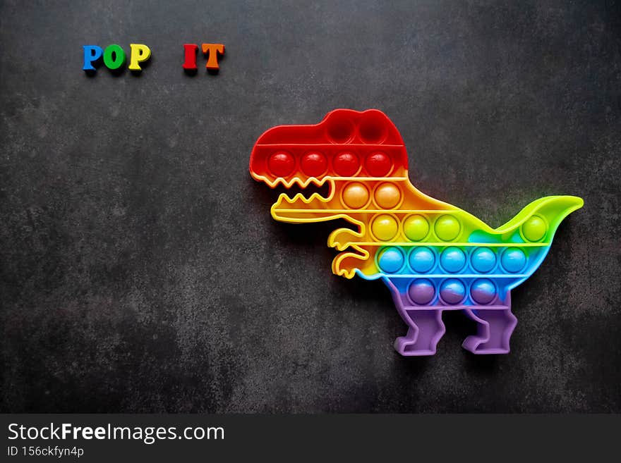 Toy pop it dinosaur rainbow colors on a black background with multicolored letters and lettering - Pop it. Copy space