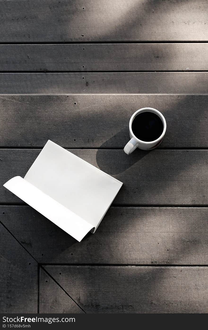 A vertical shot of a book and cup of coffee on a porch
