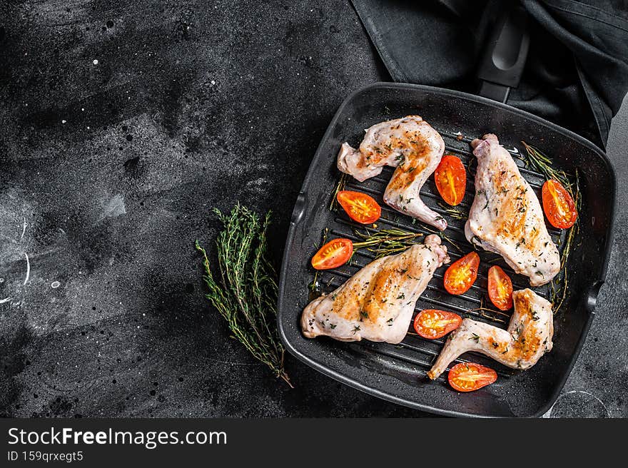 Roasted rabbit legs in a pan with thyme. Black background. Top view. Copy space.