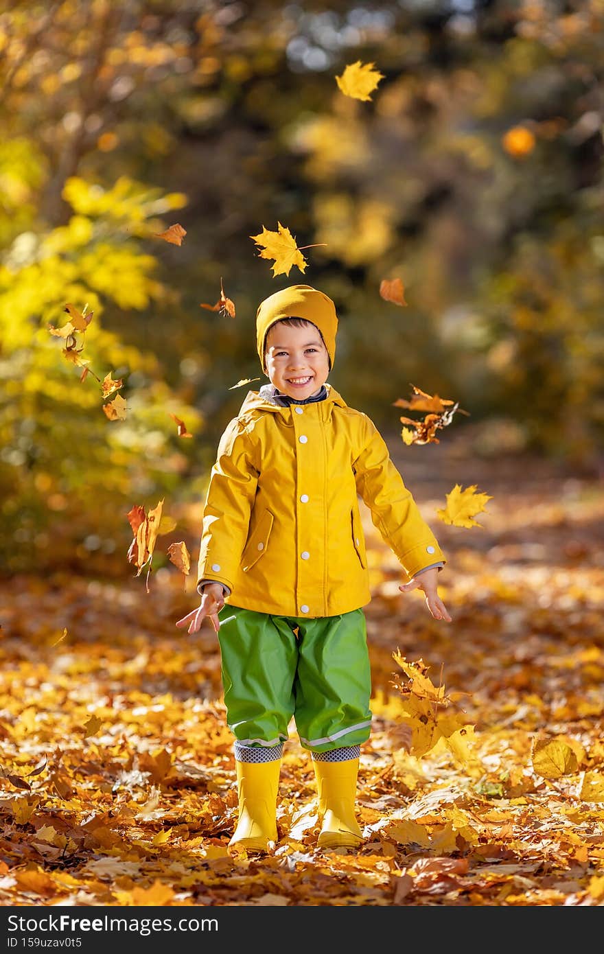 cheerful child boy in yellow raincoat and rubber boots have fun with falling leaves in autumn park. cheerful child boy in yellow raincoat and rubber boots have fun with falling leaves in autumn park