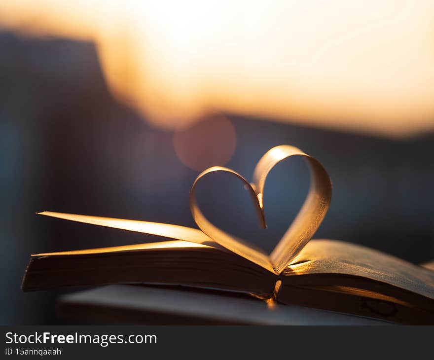 Valentine`s day, heart from a book page against a beautiful sunset.Love, valentine`s day or reading concept with heart shaped book