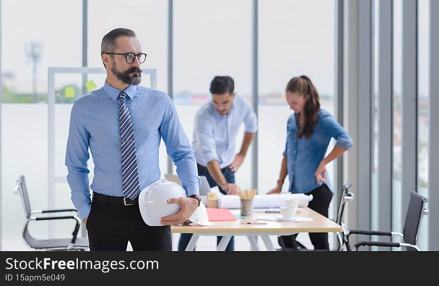 Construction engineer manager stand and holding white hardhat in front of engineers team meeting for architectural project in the