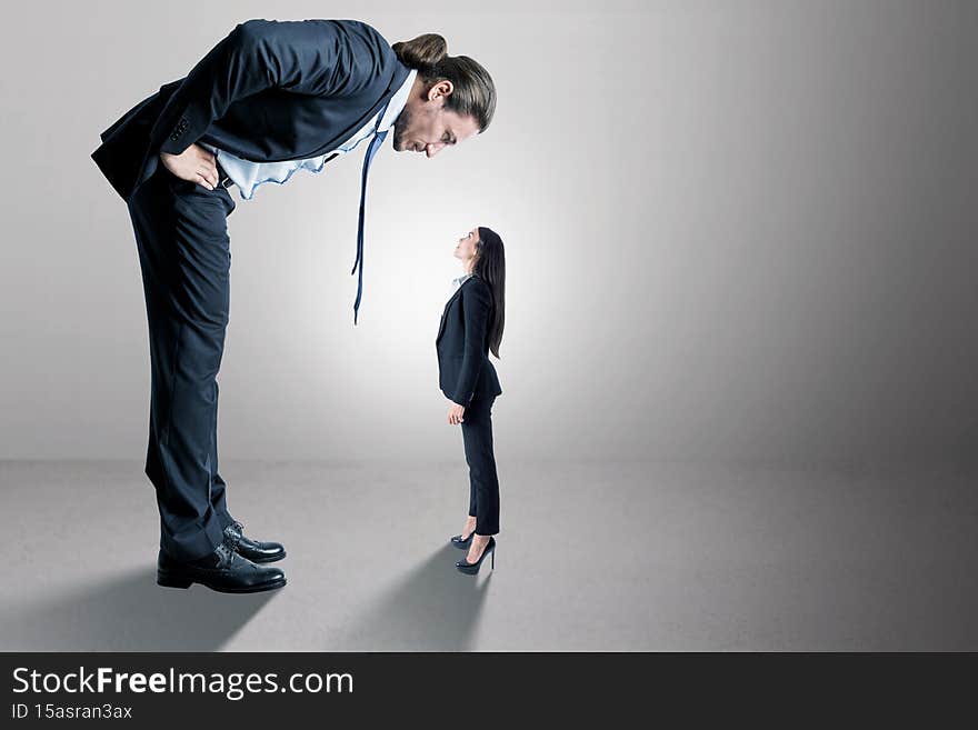 Businessman looking down on female subordinate on concrete background with mock up place for your advertisement. Boss and discrimination concept