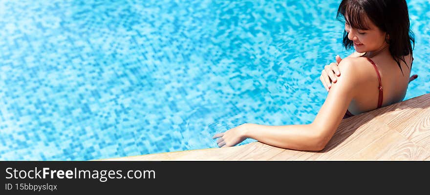 Beautiful Asian women in swimming wear while standing to relax in the pool and not being afraid of UV effects of sun on the skin