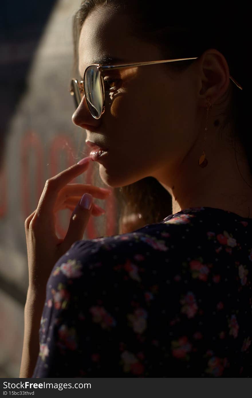 Close-up portrait of stylish young woman. Brunette in sundress posing on street. Finger near her lips. Close-up portrait of stylish young woman. Brunette in sundress posing on street. Finger near her lips