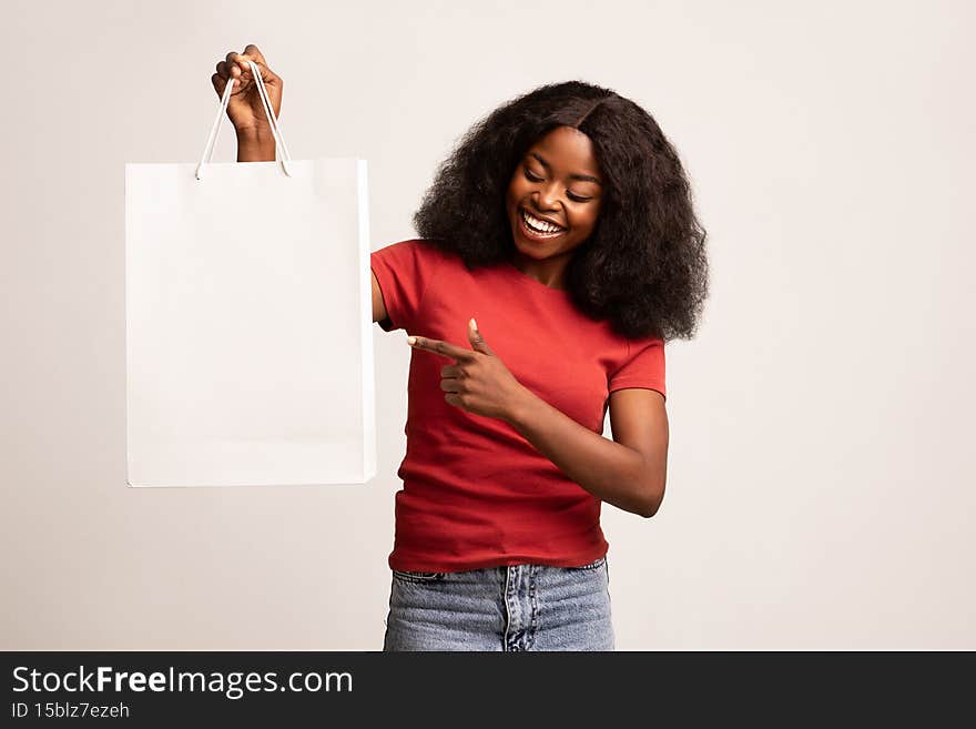 Place For Design. Cheerful Black Woman Holding And Pointing At Blank Paper Shopping Bag, Happy Young African American Shopaholic Lady Demonstrating Copy Space For Your Advertisement, Mockup. Place For Design. Cheerful Black Woman Holding And Pointing At Blank Paper Shopping Bag, Happy Young African American Shopaholic Lady Demonstrating Copy Space For Your Advertisement, Mockup