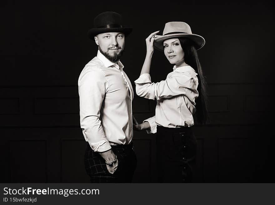 A men and a women in white shirts and hats on a black background.A couple in love poses in the interior of the studio.black and white photo. A men and a women in white shirts and hats on a black background.A couple in love poses in the interior of the studio.black and white photo.