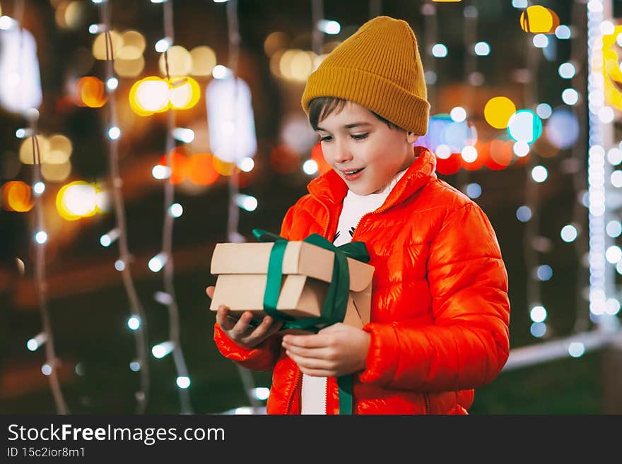 Portrait of a happy boy standing on the evening street and opening a Christmas gift. Christmas gifts, holiday atmosphere