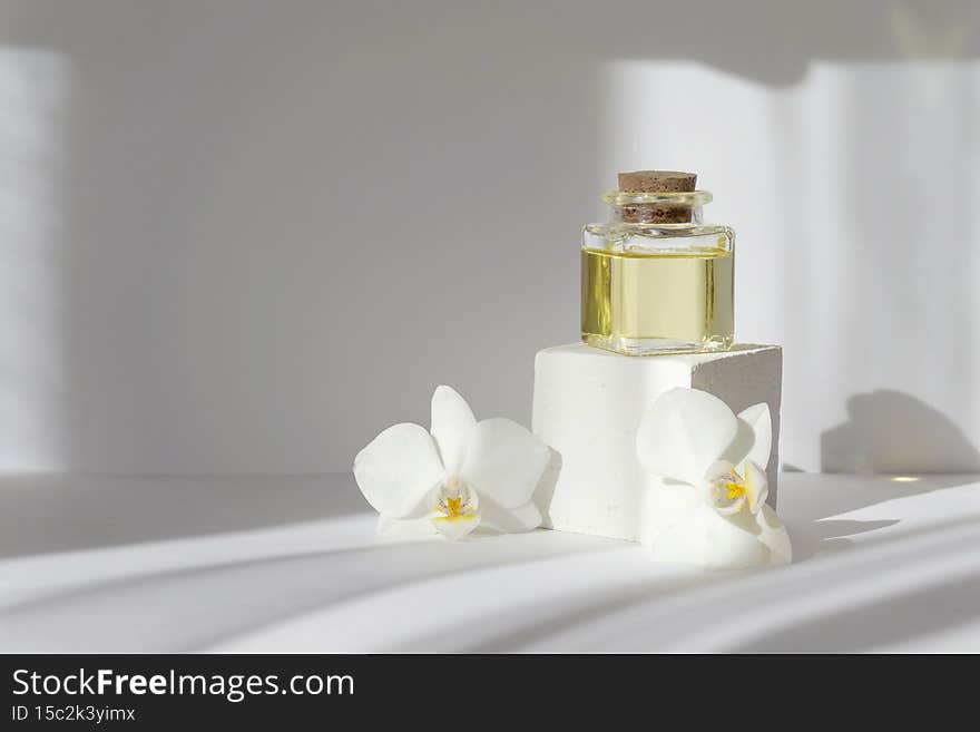 Mock-up of square bubble with essential oil on white 3d podium, surrounded by orchid flowers. Objects in rays of sunlight cast hard shadow on surface. Concept of spa treatments, body care.