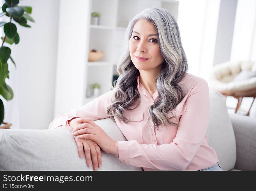 Photo of attractive aged woman happy positive smile curly hair confident dream sit couch relax indoors.