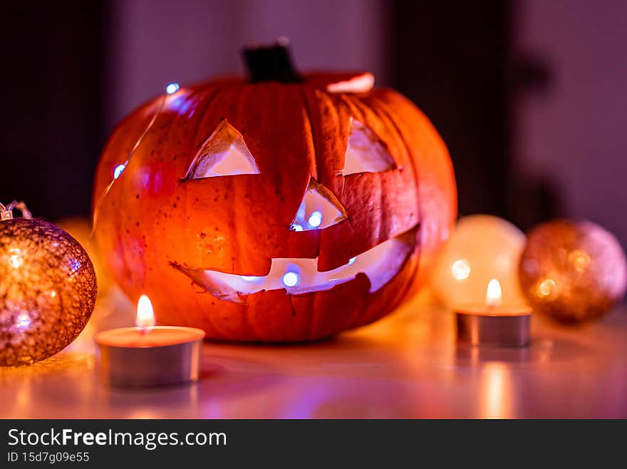 Spooky smiling halloween pumpkin in burning fire candles flames. The big Halloween symbol has a mad face glowing eyes mouth and glow teeth surrounded by candies.