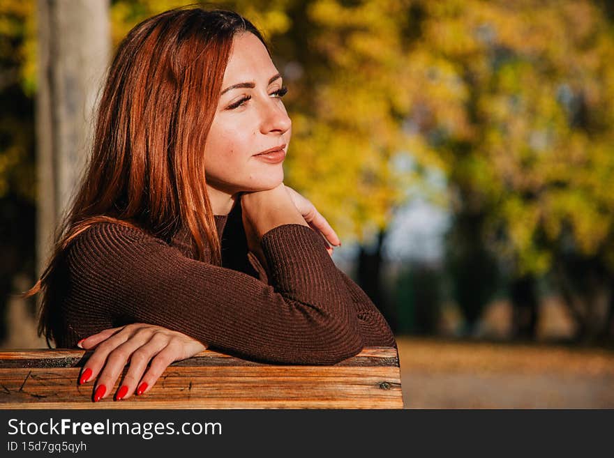 A young, red-haired girl sits in an autumn park on a bench. High quality photo