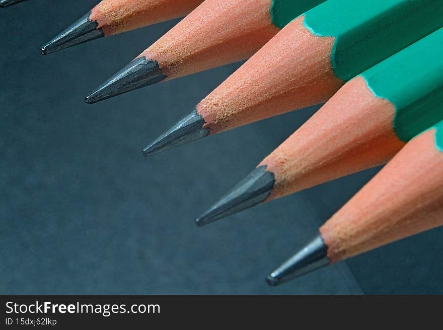 Green sharpened wooden pencils with black lead on a dark textured background. close-up