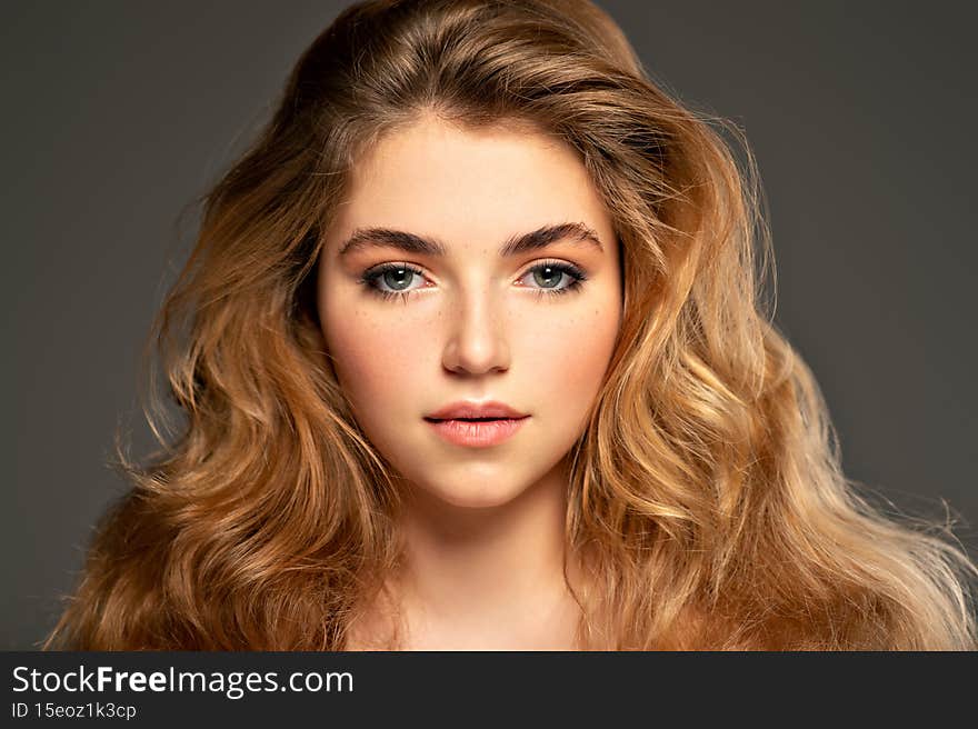 Closeup portrait of an young adult girl with long curly hair.  Photo of a fashion model posing at studio. Pretty young woman with