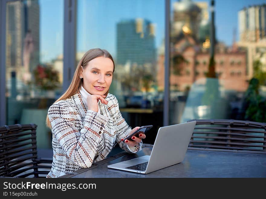 Blonde caucasian woman freelancer is working with her project on laptop remotely from a city cafe outdoors
