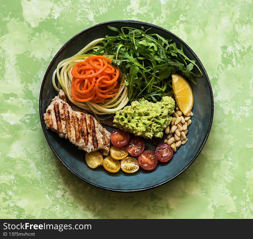Balanced food concept. Buddha bowl salad with grilled chicken breast, arugula, avocado, carrots and zucchini, balanced clean eating, top view. Healthy lunch bowl